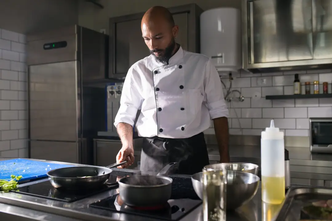 Profesyonel mutfakta beyaz aşçı ceketiyle yemek hazırlayan şef