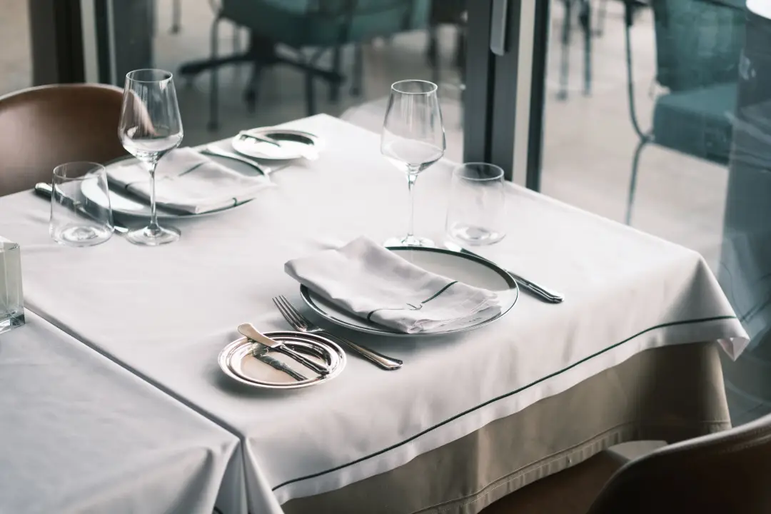 Beyaz masa örtüsü ve katlanmış kumaş peçetelerle hazırlanmış şık restoran masası